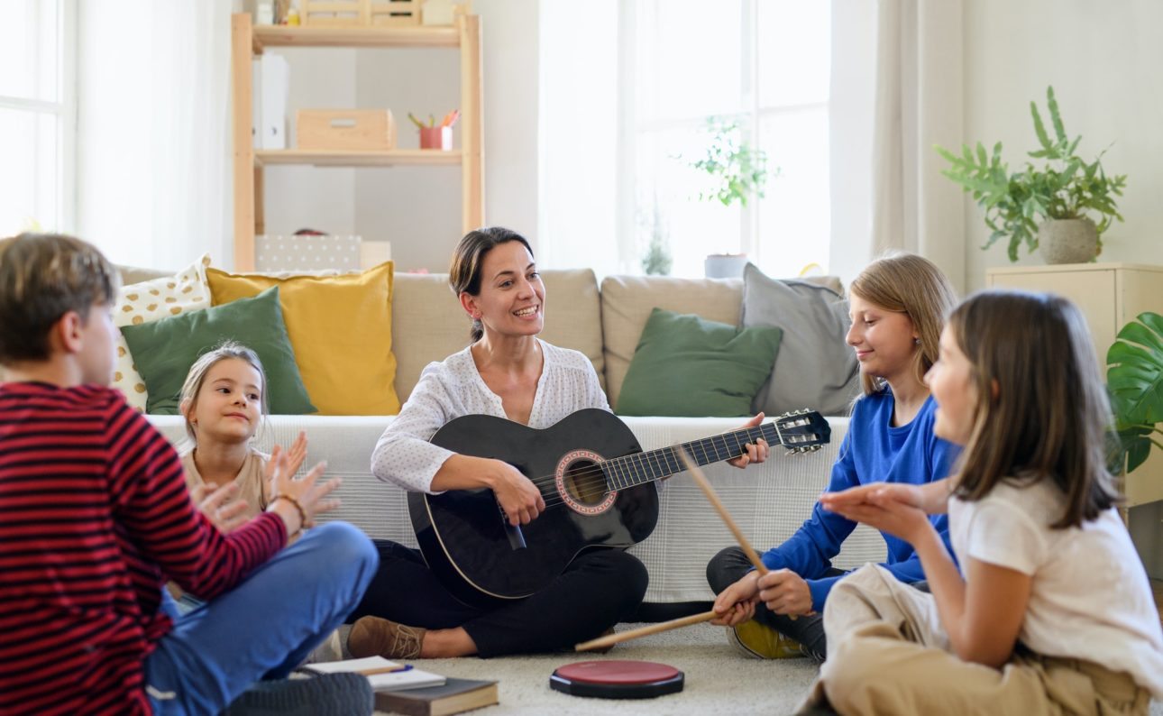 Group of homeschooling children with teacher having music lesson indoors, coronavirus concept.